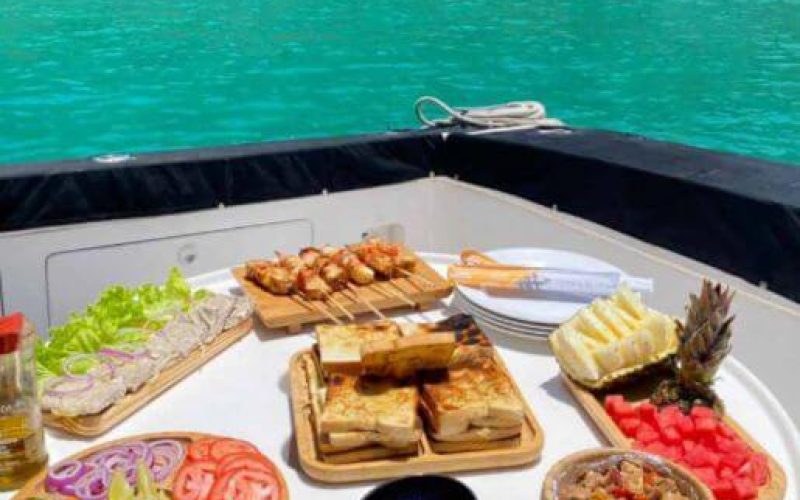 Lancha do Trovão com churrasco a bordo, navegando pelas águas de Fernando de Noronha, ao fundo, o mar cristalino e paisagens deslumbrantes.