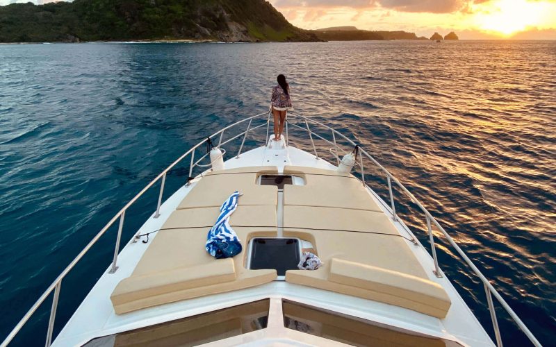 Lancha do Trovão no pôr do sol em Fernando de Noronha, com mar dourado e Morro Dois Irmãos ao fundo